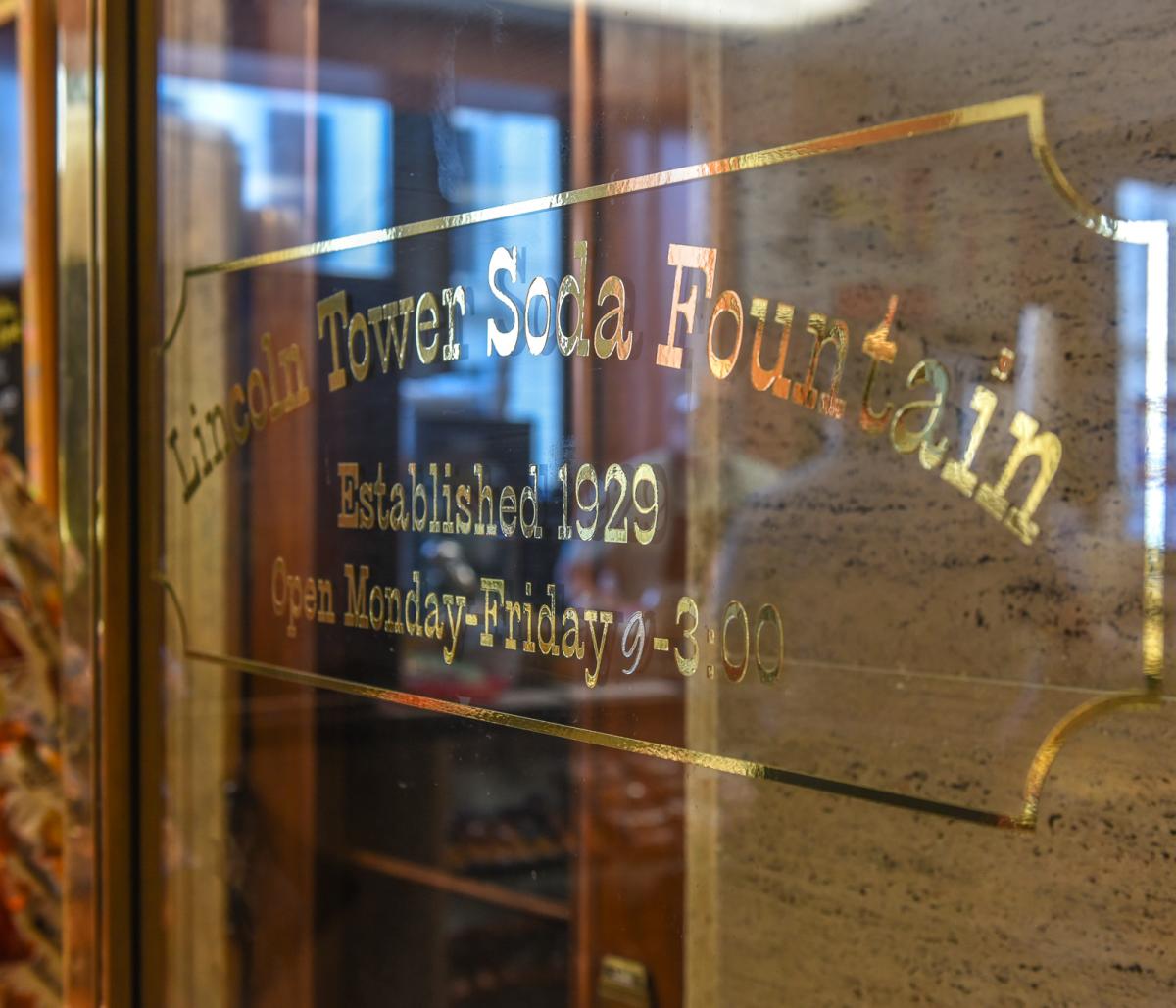 Gold letters writing "Lincoln Tower Soda Fountain" are on a glass door