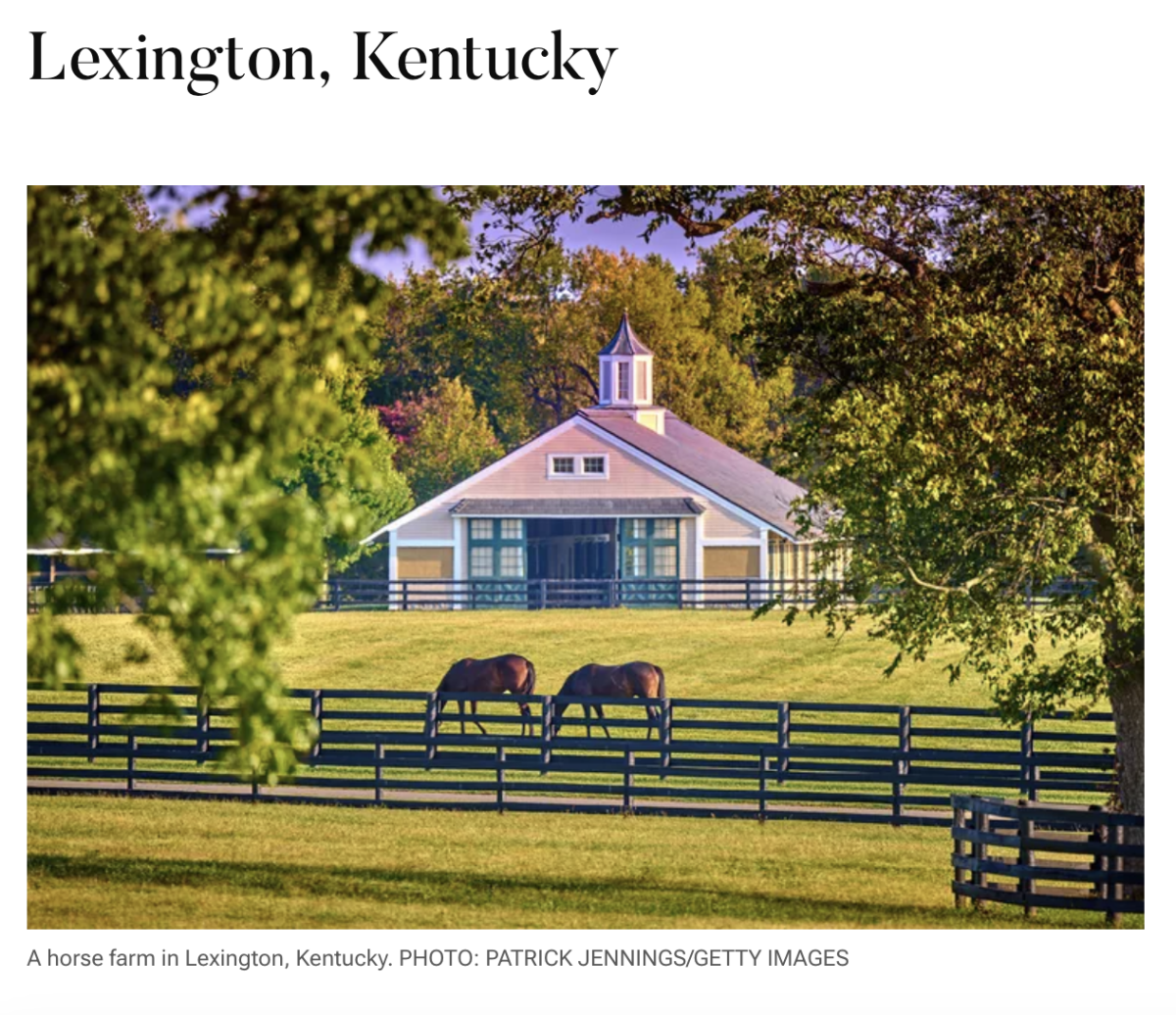 Two horses grazing with barn and wooden fence