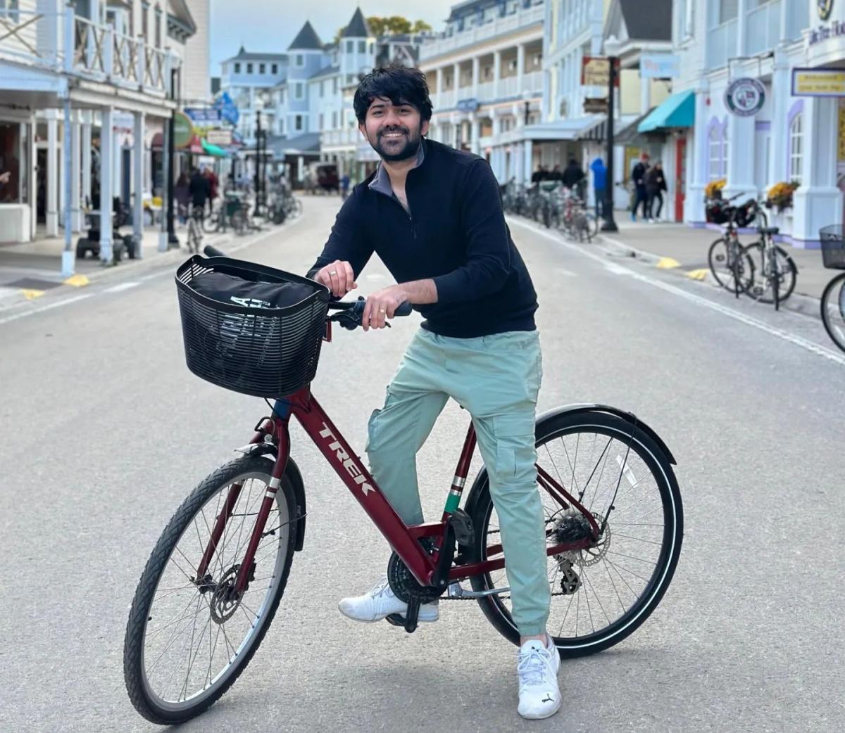 A smiling man sits on a bicycle in the middle of Mackinac Island’s Main Street