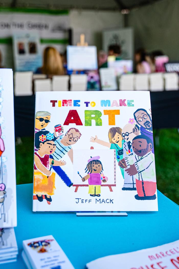 A close-up of a book propped up on a table at Books on The Green (during The Woodlands Waterway Arts Festival). The book is called "Time to Make Art," and the cover depicts a cartoon-like figures of different kinds of artists (painters, photographers, florists, etc.).