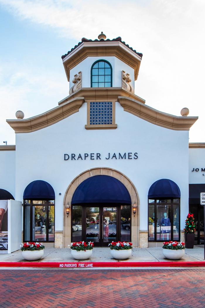 The Draper James building at Market Street is tall and white with a turret-like structure over the front entrance. The roof and turret are lined in gold-colored stone. The face of the building features royal blue awnings and blue tile accents.