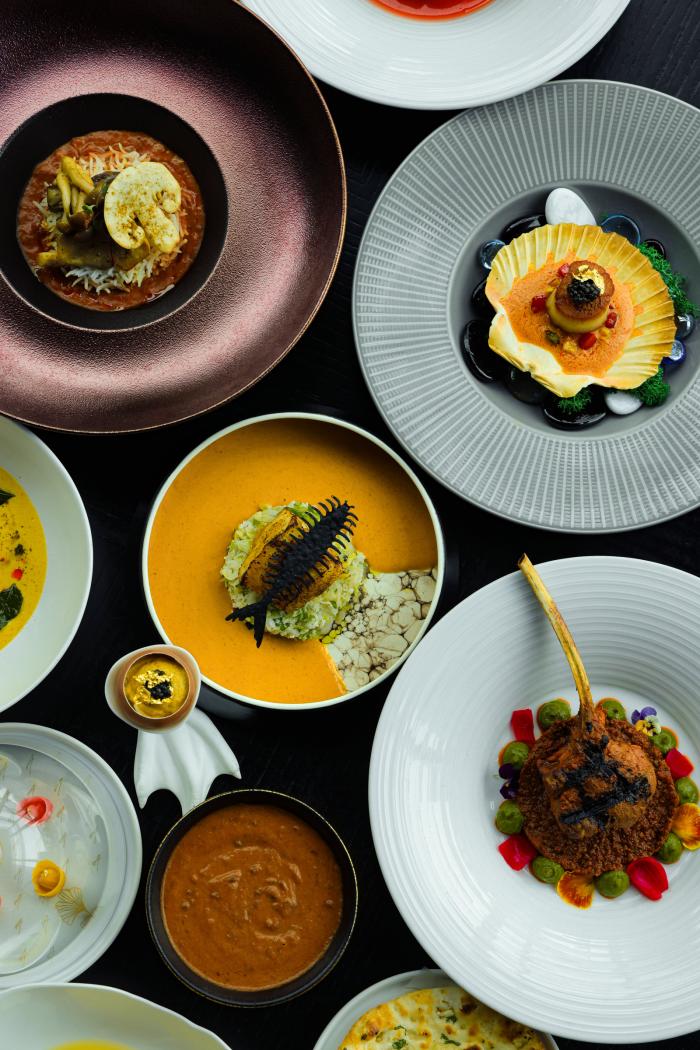 An overhead view of an elegant tasting menu from Amrina. Every dish and the flatware is different, some featuring mushrooms, curry, seafood, steak, or naan bread.