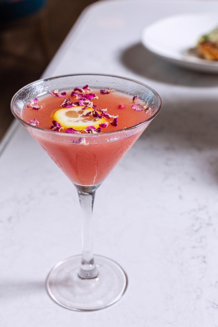 A rose water lemon drop at The Audrey is a pink drink garnished with a lemon slice and dried rose petals.