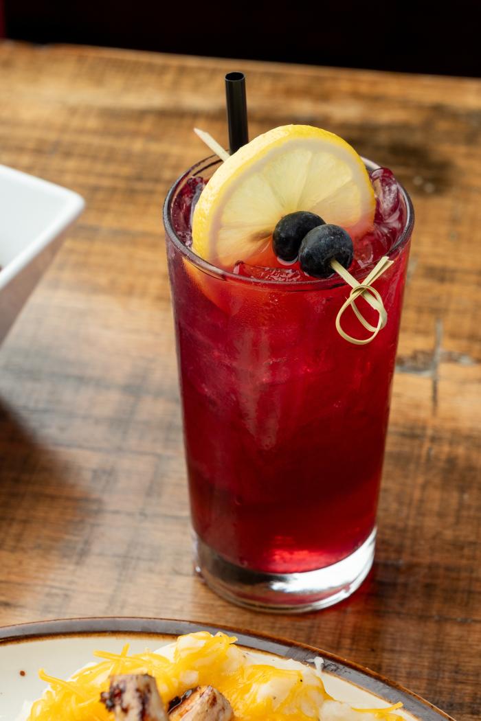 A clear glass of a bright red drink, topped with blueberries and a lemon slice.