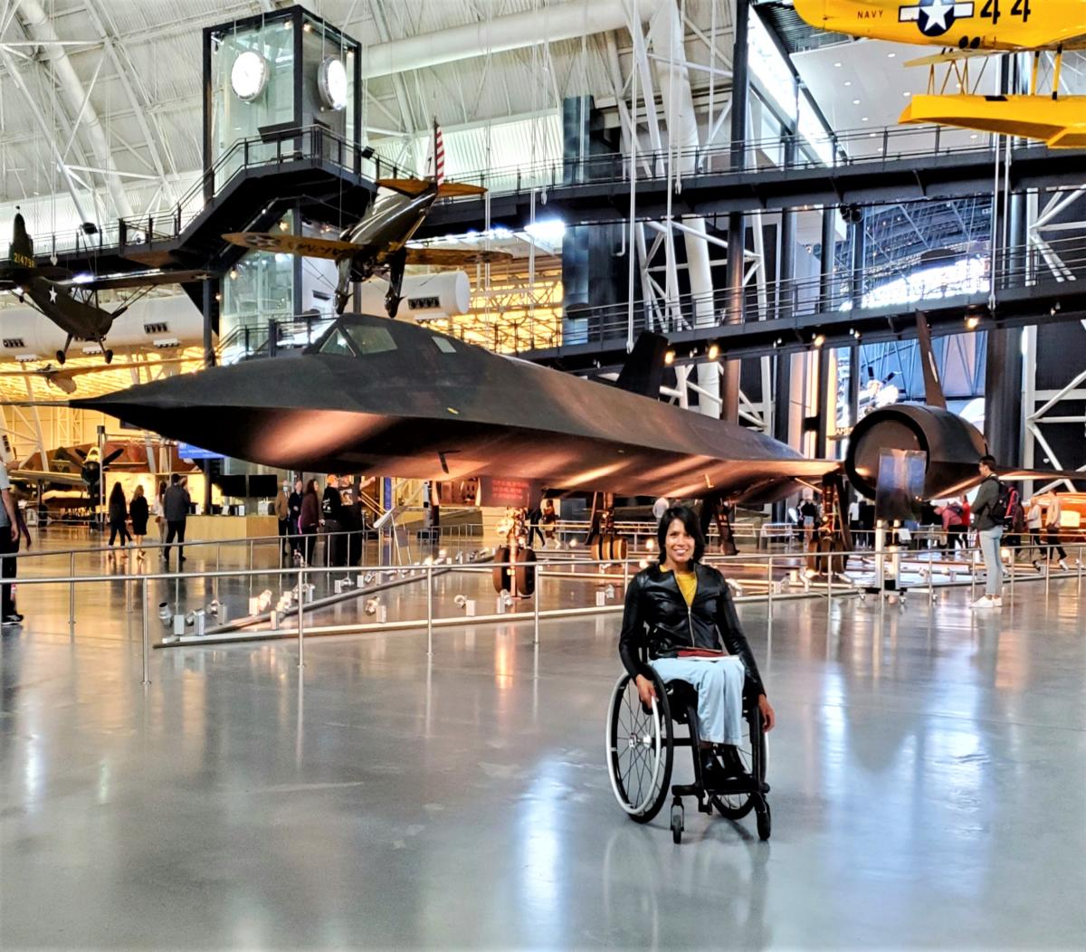 Woman in wheelchair posing in front of black reconnaissance jet at Air and Space Museum