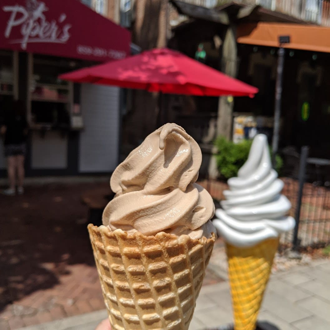 A chocolate soft-serve twist cone in front of a statue of a white soft serve cone in front of Piper's Ice Cream in Mainstrasse Village in Covington, Ky.