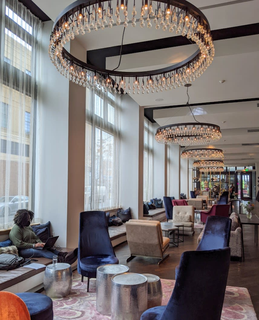 A woman using her laptop in the lobby of Hotel Covington, with blue velvet chairs lining the lobby and chandeliers overhead.