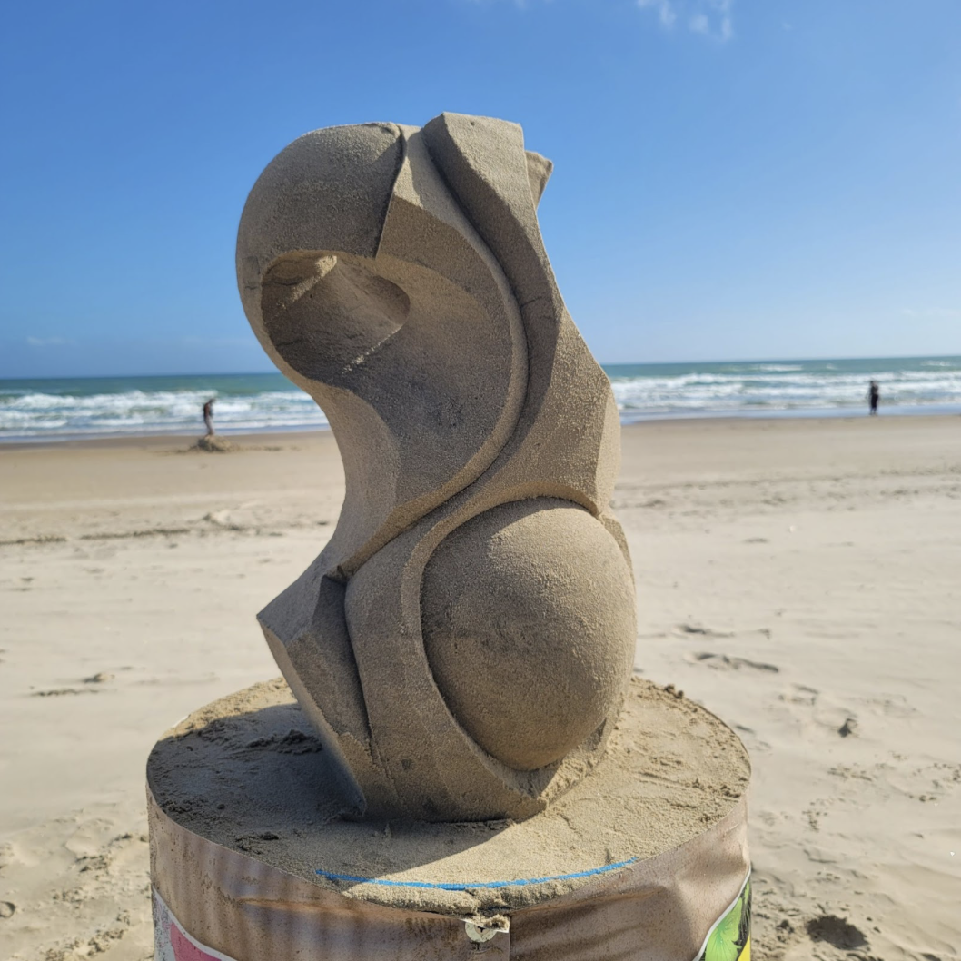 A smooth geometric sand sculpture on top of a platform on the beach.