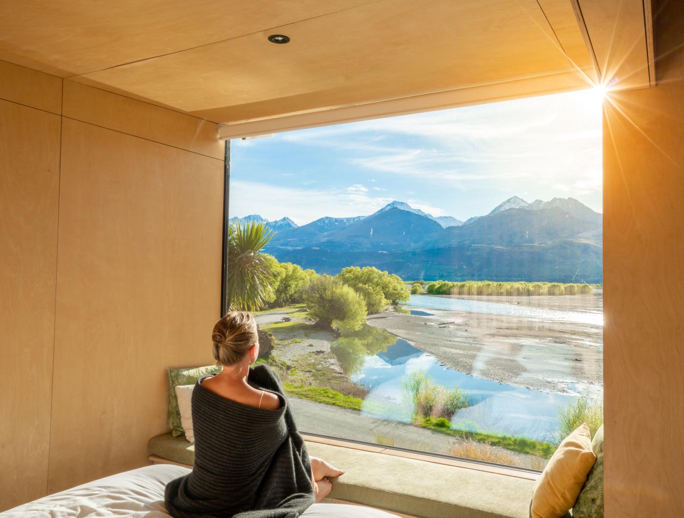 Woman looking out a huge window with view of mountains and lake at Kinloch Wilderness Retreat