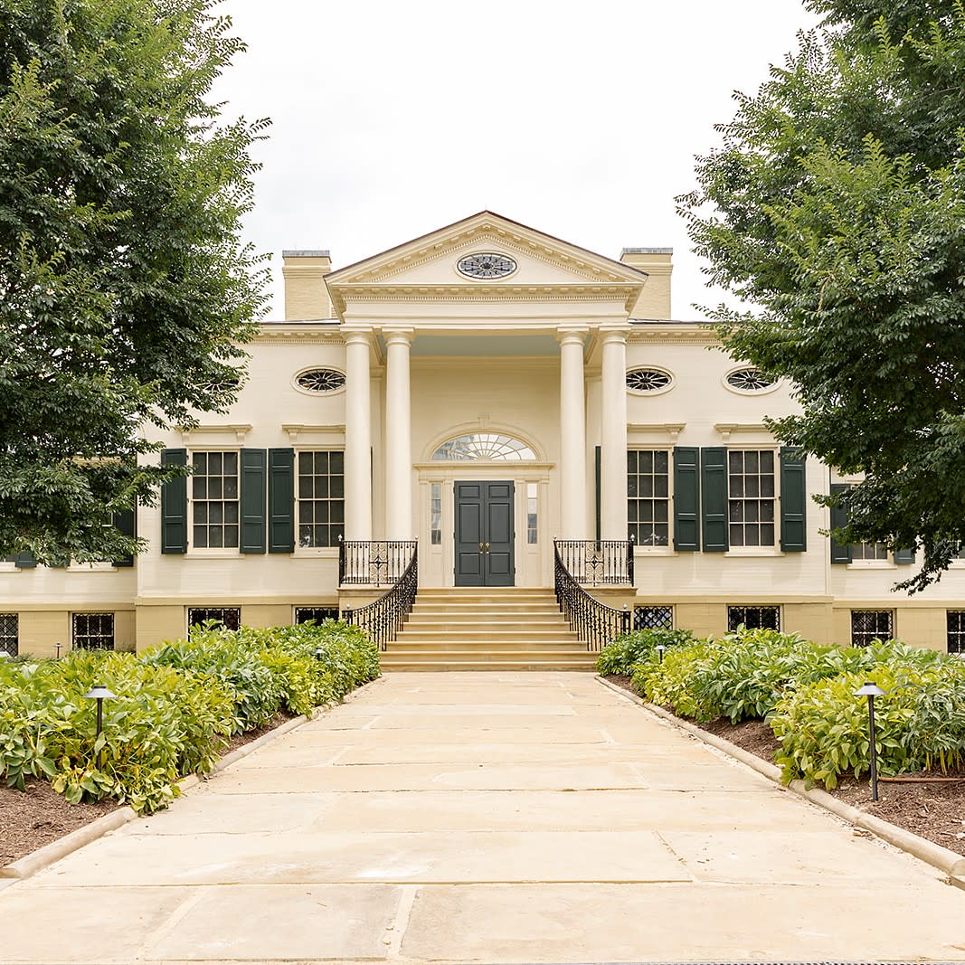 Image is of the front of the Taft Art Museum building with tree's on either side during the summer.