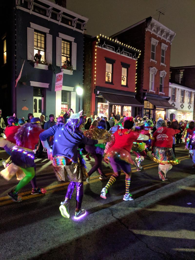 People in bright colors wearing light up shoes and other lights in the Mainstrasse Village Mardi Gras parade