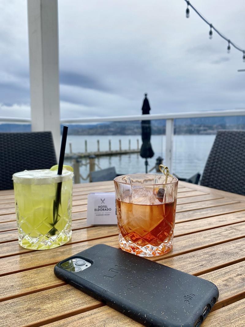 Two mixed drinks and a cell phone sit on an outdoor table overlooking the water at the Lakeside Restaurant at Hotel Eldorado