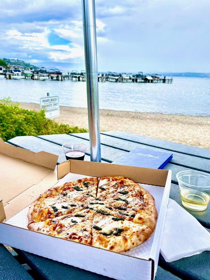 A whole pizza sitting in an open box on an outside table next to the water at Frind Winery