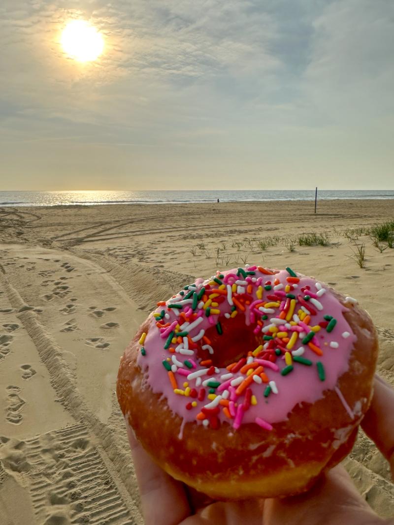 Hand holding doughnut on Sandbridge Beach watching sunrise