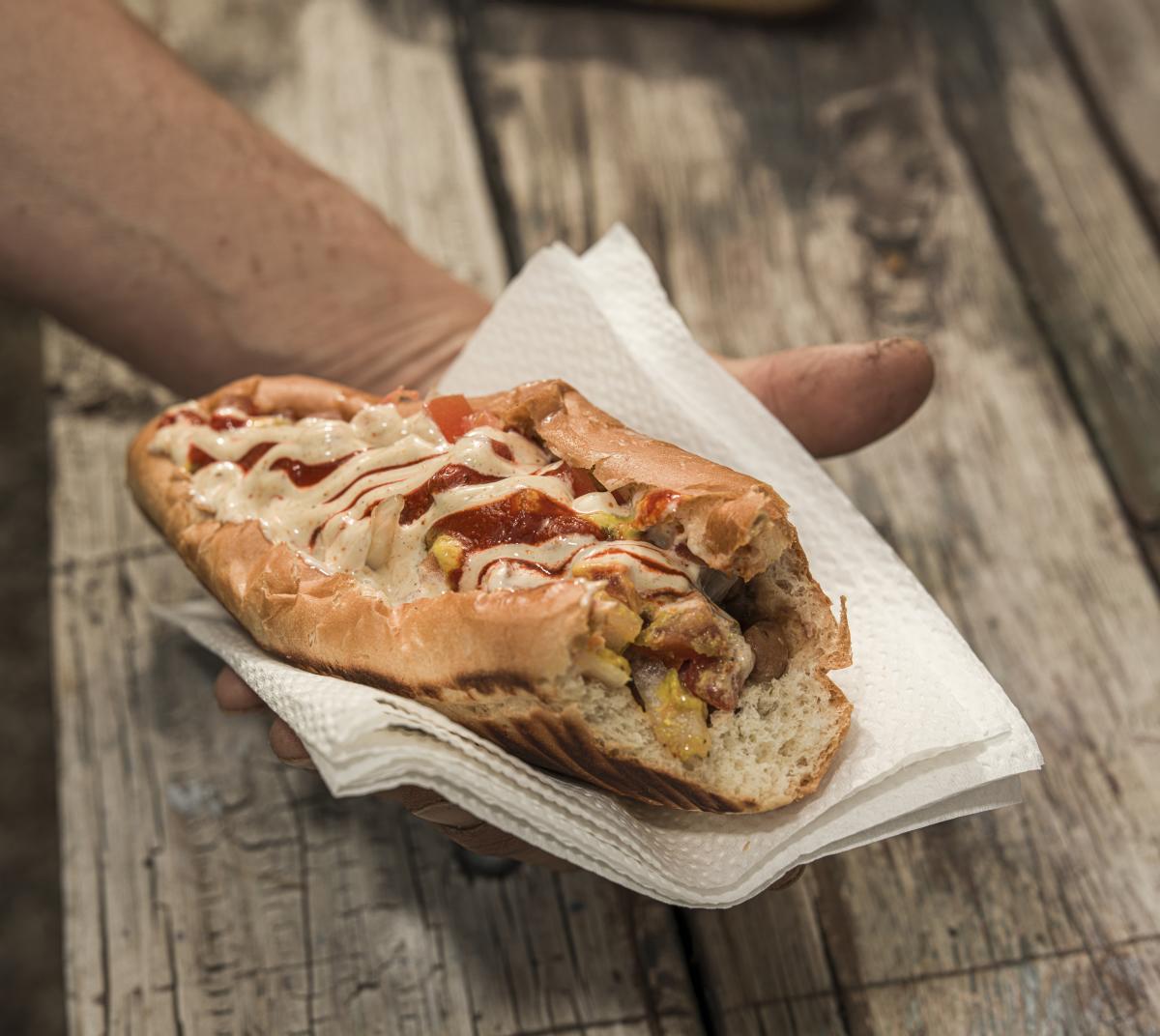A close-up of a Sonoran-style hot dog wrapped in bacon and nestled into a soft bun, covered with toppings.