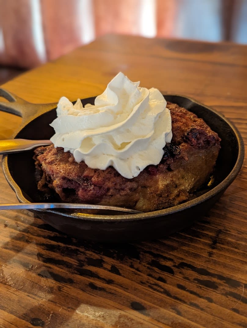 Image is of the mixed berry bread pudding with whipped cream on top in a small cast iron skillet.