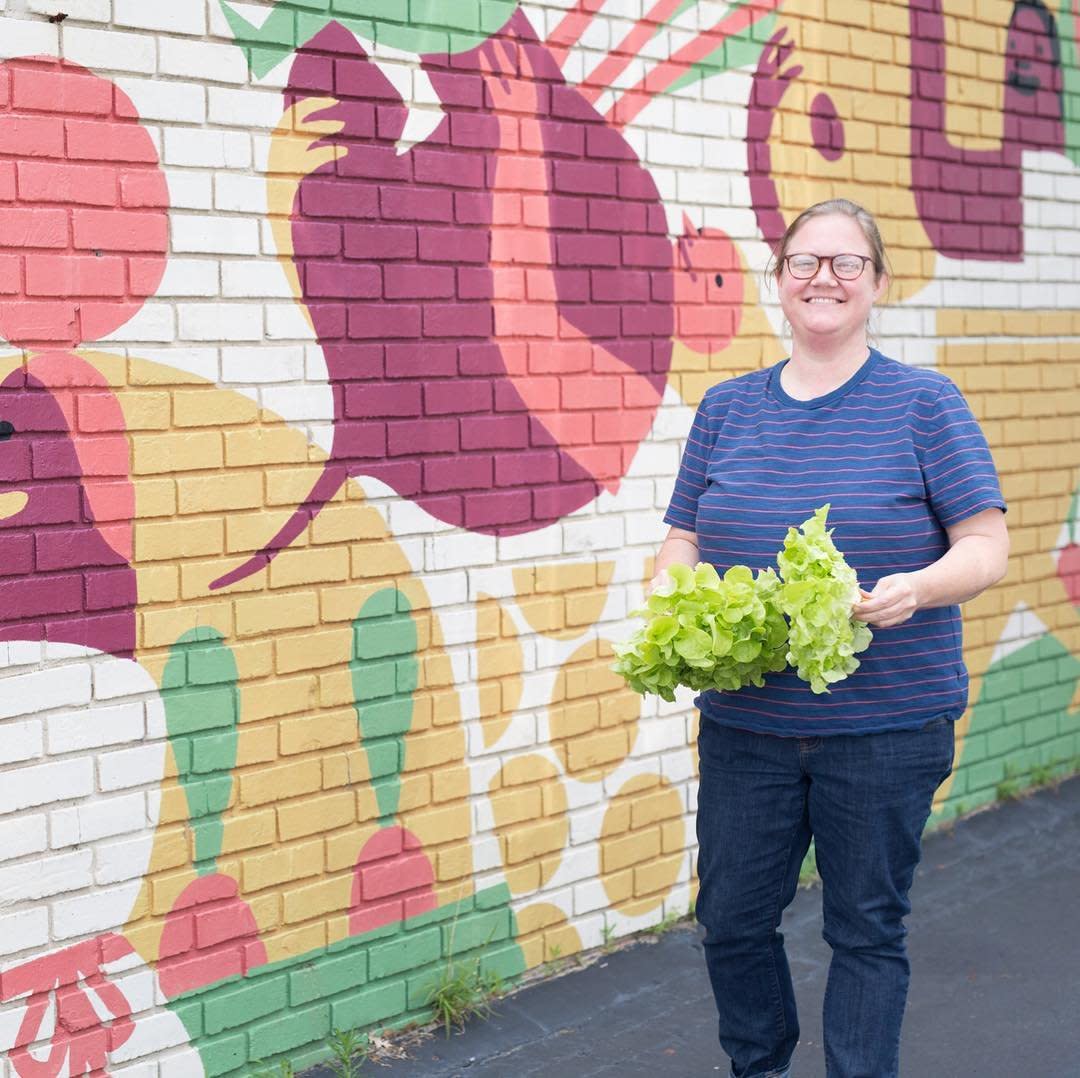 Mimi Maumus of home.made stands in front of a colorful mural, holding vegetables.