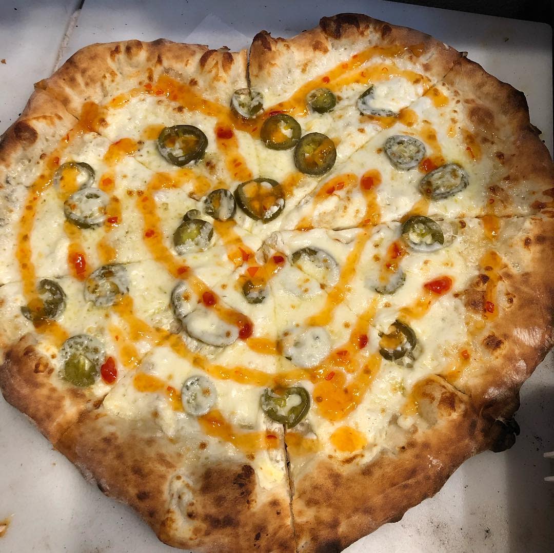 Heart-shaped pizza with cheese, jalapenos, and hot sauce.