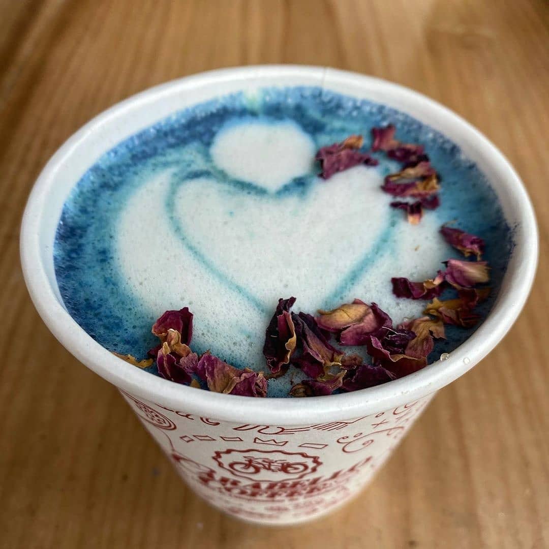 Image is of a blue cappuccino with a heart in the foam and dried flowers floating.