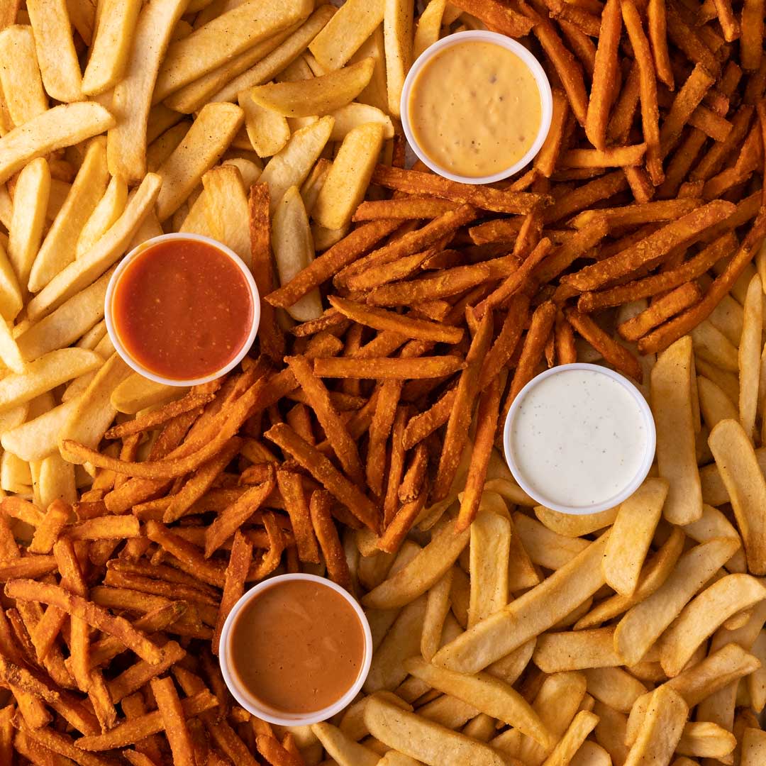 An image of steak fries and sweet potato fries with 4 little cups filled with different sauces in the middle of it.