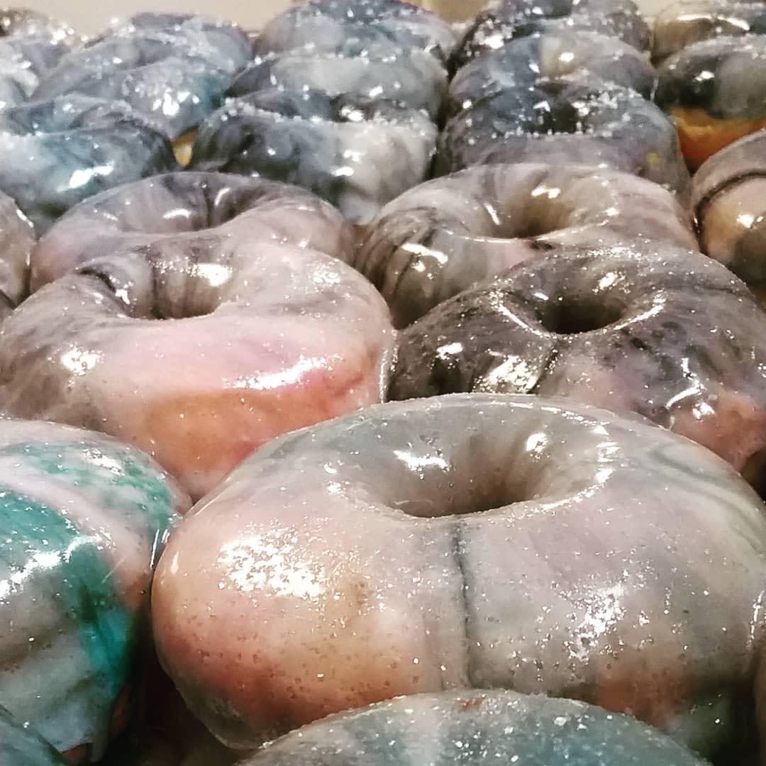 Closeup of a tray packed with doughnuts iced with pink, blue and purple icing at Moonrise Doughnuts