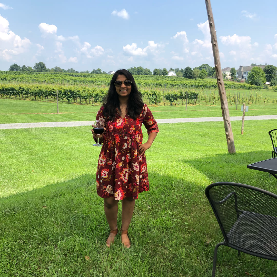 A young woman wearing a flowered dress stands outside in front of rows of vines at Fabbioli Cellars in Lucketts, VA