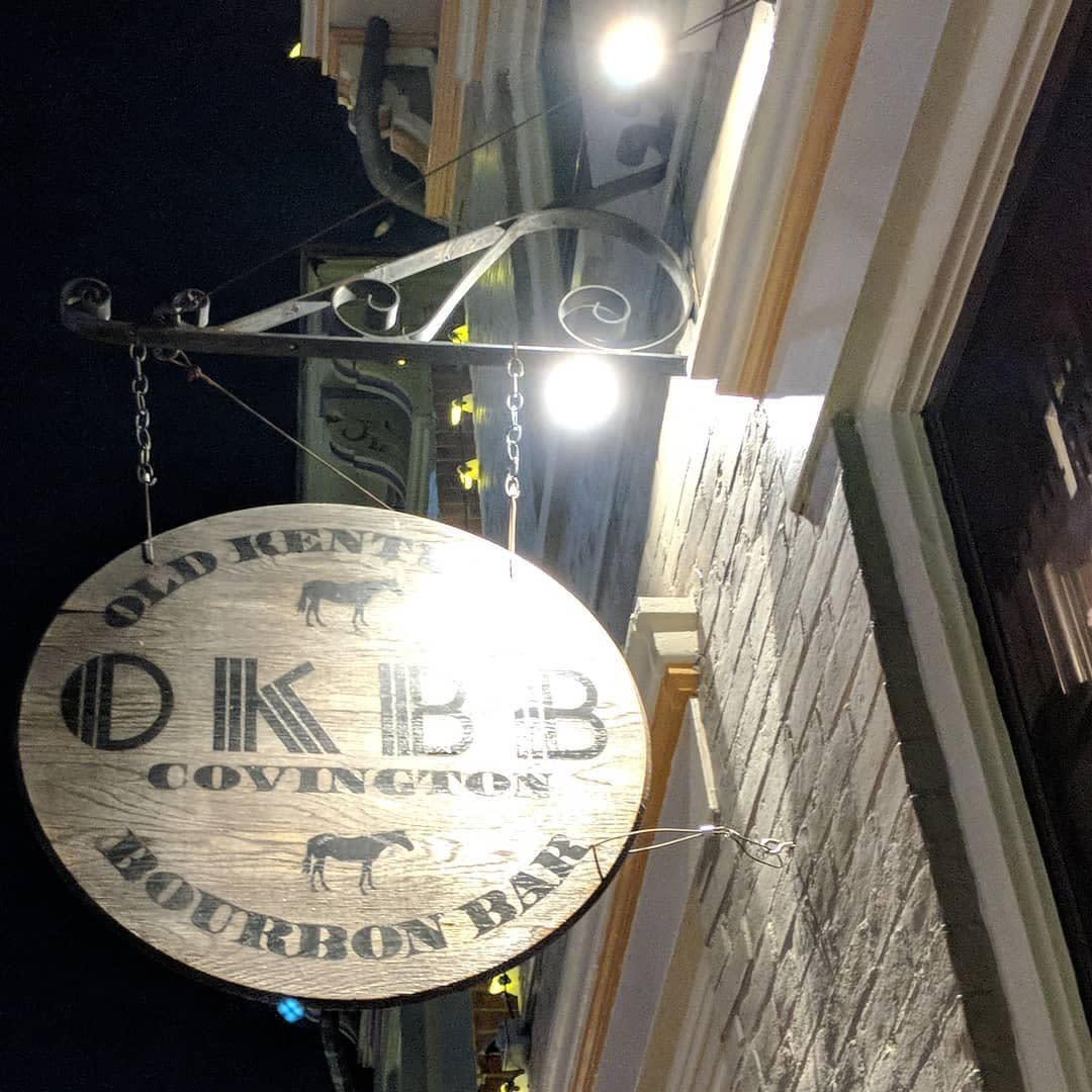 Round wood sign for OKBB, Old Kentucky Bourbon Bar, hanging by brick wall