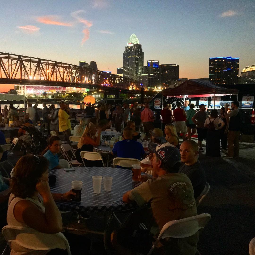 sunset at dusk with bridge and people enjoying drinks around a table during newport oktoberfest in newport ky