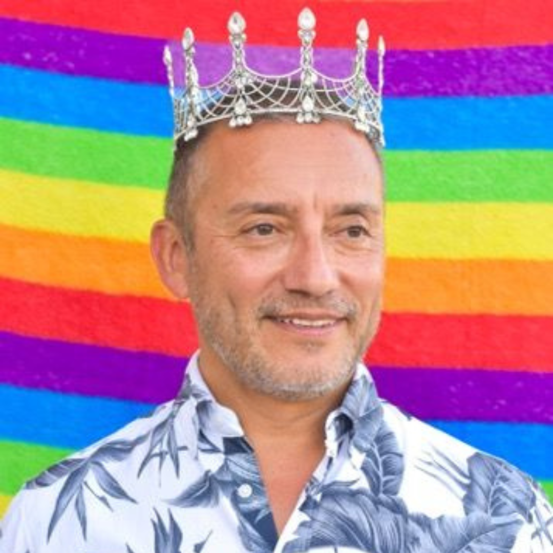 Man in crown in front of rainbow backdrop