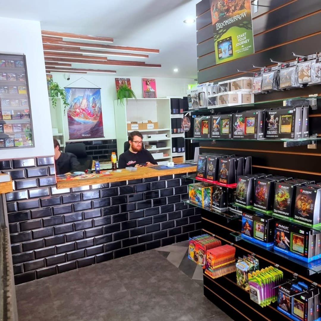 Man sat behind front desk nearby a wall of trading card games inside Dice & Dumplings