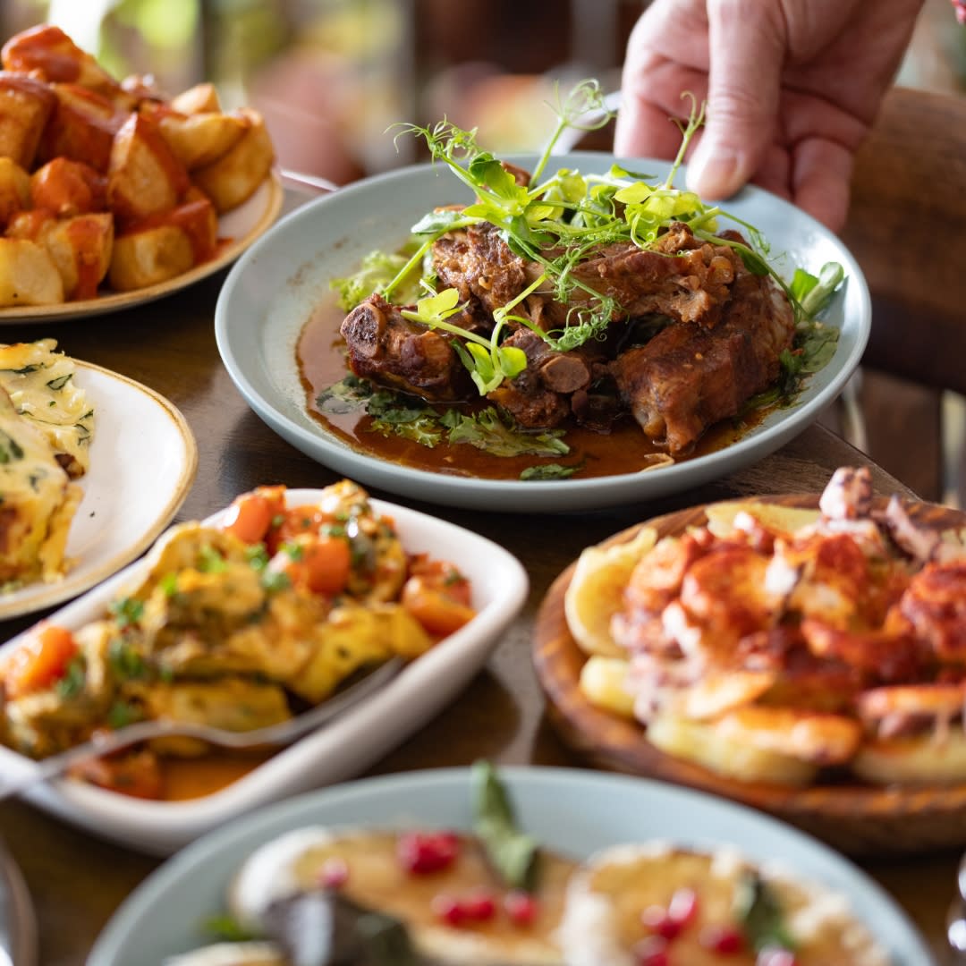 Range of spanish tapas dishes being placed on a wooden table including patatas bravas and pork ribs