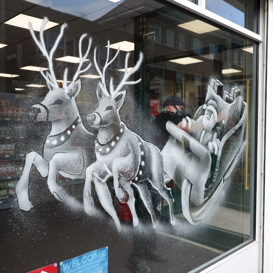 Artist Tom Baker finishing snow windows design of Santa and his sleigh with two reindeer in a shop window