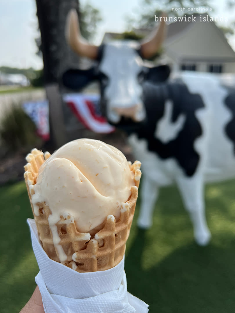 a scoop of peach ice cream on a waffle cone pictured in front of a cow statue at the Calabash Creamery