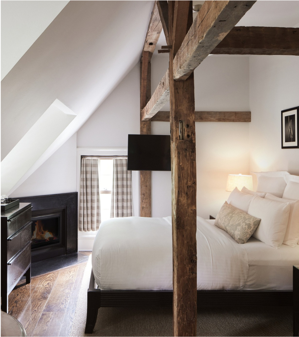 A guest room at the Bedford Post Inn. The room has wooden beams going over the bed and a fireplace can be seen in the background.