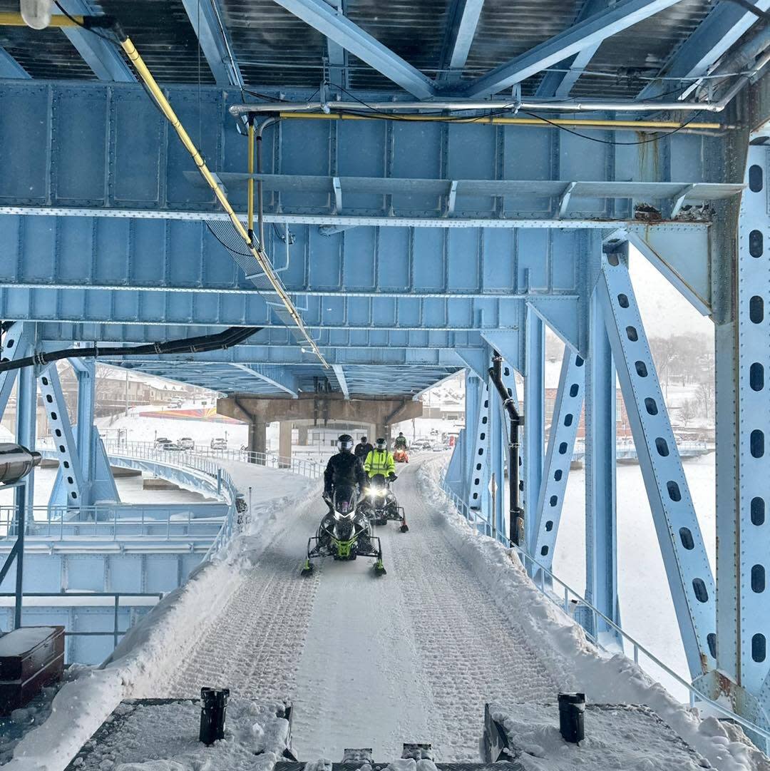 Snowmobilers cross lift bridge.