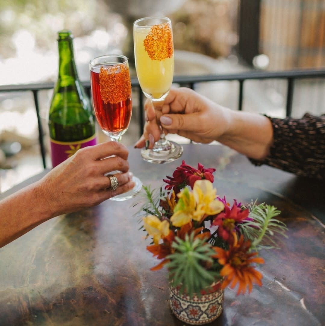 two hands cheersing mimosa glasses