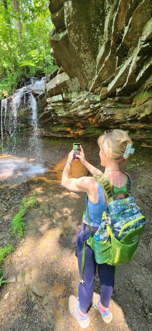 A hiker with a backpack takes a photo of a waterfall cascading over a rocky ledge along a wooded trail on Monte Sano in Huntsville, Alabama.
