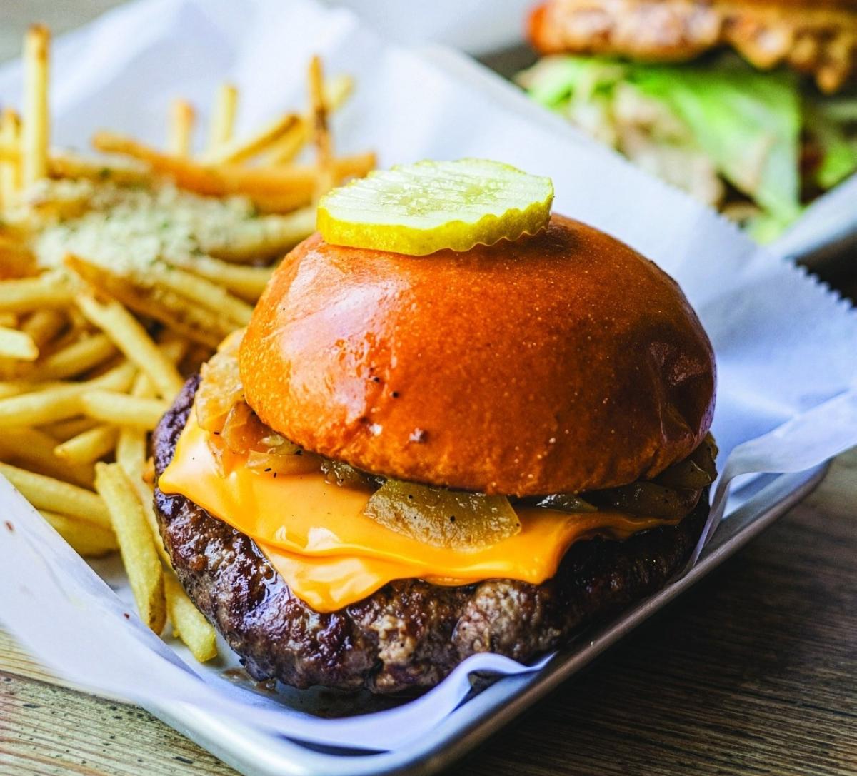 Cheeseburger topped with melted cheese, grilled onions and pickles, served with french fries in a paper-lined tray.