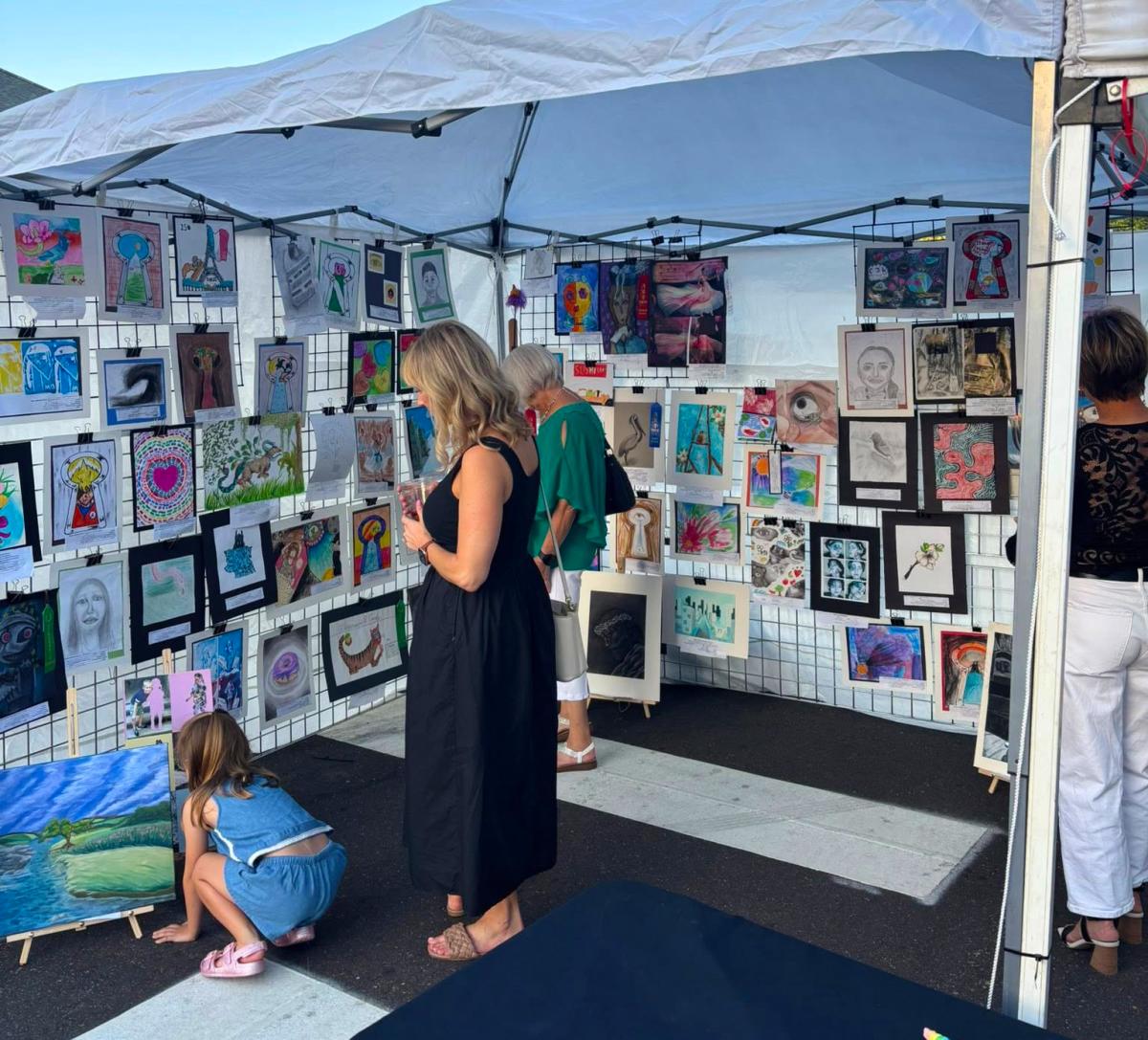 Visitors browse colorful artwork displayed in a St. Tammany Art Association booth during a downtown Covington arts event.