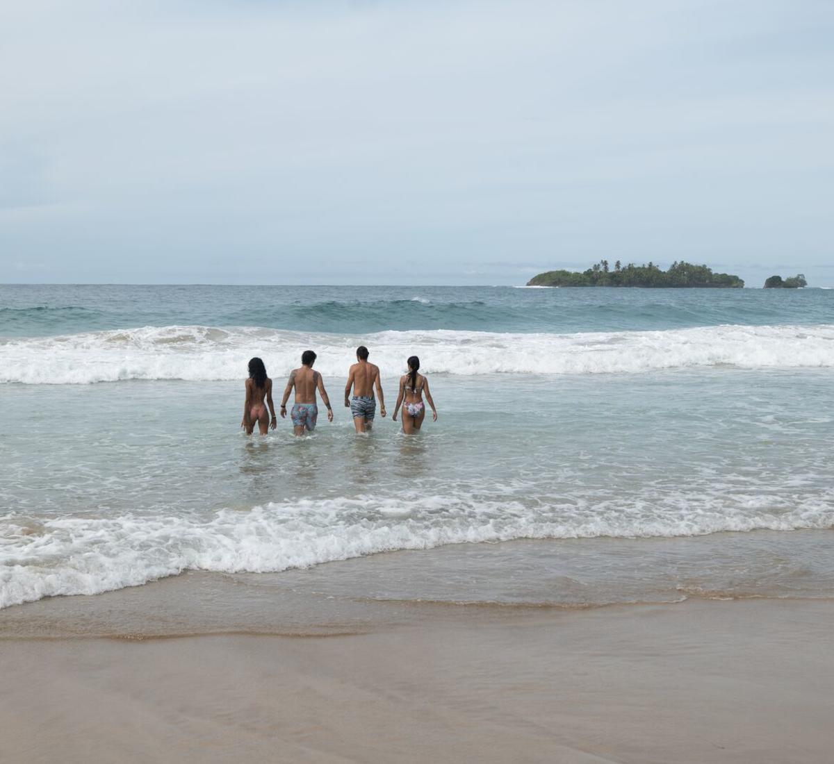 Turistas entrando al mar en una playa de Isla Bastimentos con una pequeña isla al fondo