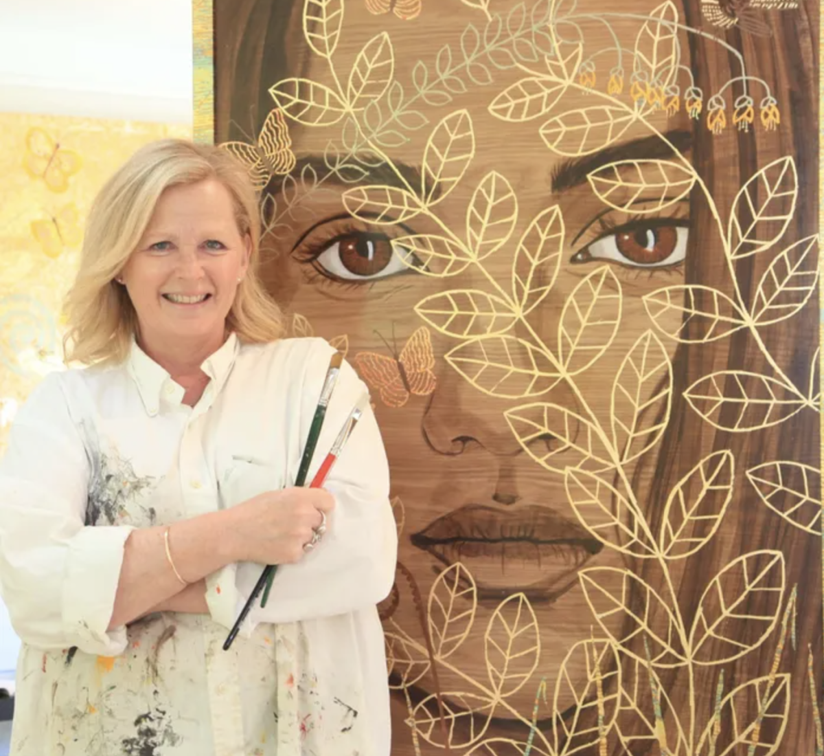 Artist Jenny Merhtens in front of a painting of woman with golf leaf pattern