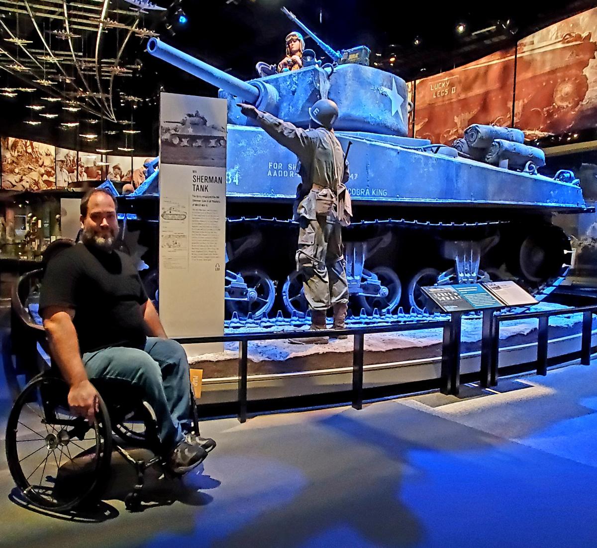 Wheelchair user posing next to the actual Sherman military tank used in World War II at the National Museum of the U.S. Army in Fairfax County, VA