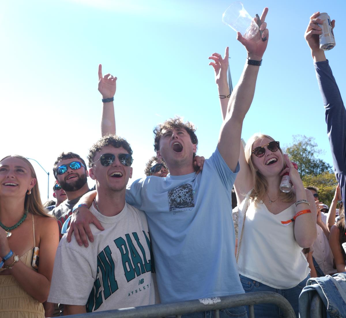 Standing in a cheering crowd, two Caucasian men stand together, cheering.