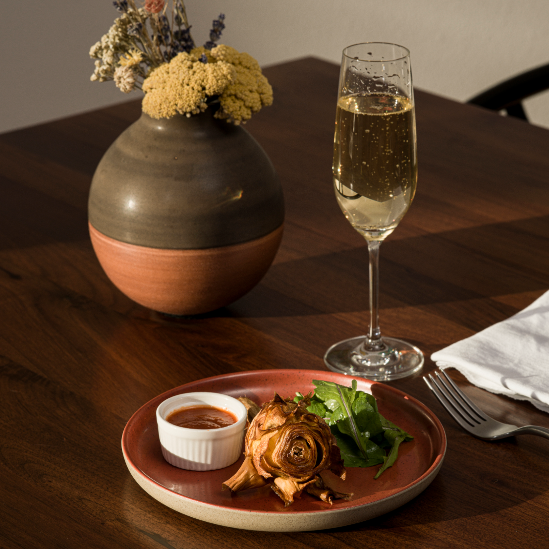 A plate of crispy fried artichokes next to a glass of Champagne on a simple, elegant table.