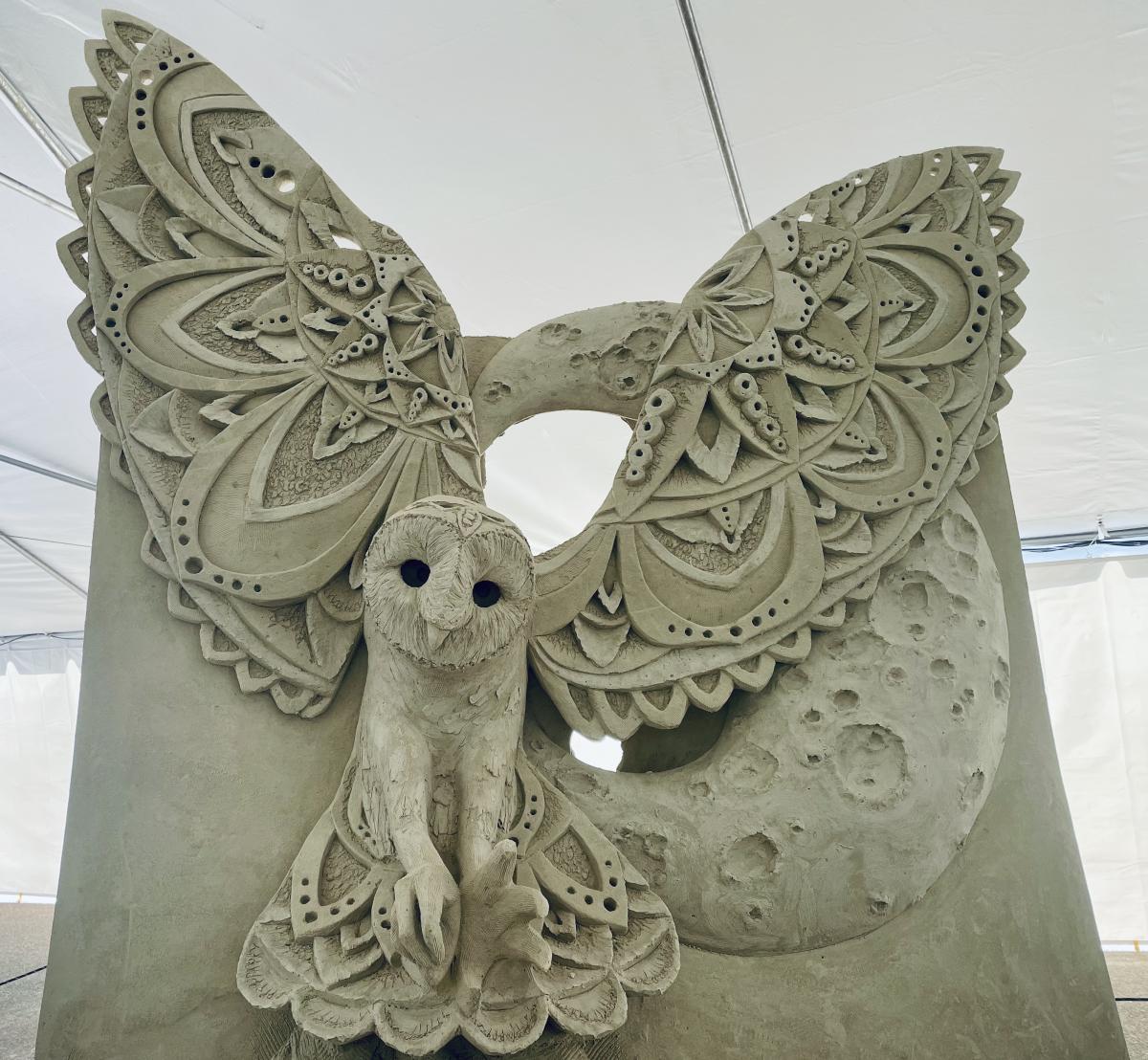 Sand sculpture under a tent depicting a flying owl with intricate wings