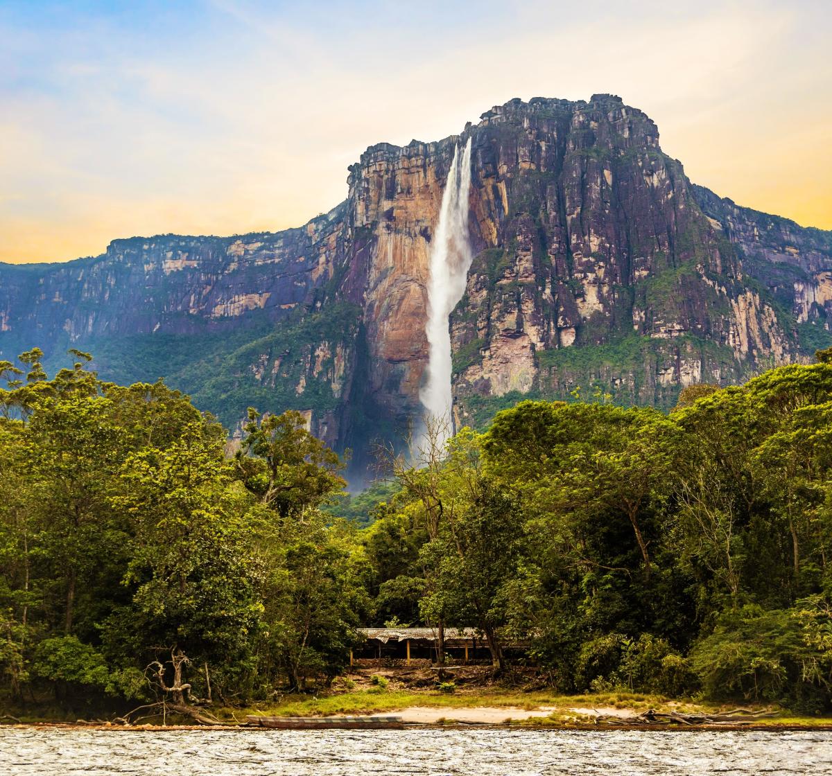 A towering waterfall, known as Angel Falls in Venezuela, plummets from a flat-topped mountain, surrounded by lush, green jungle.