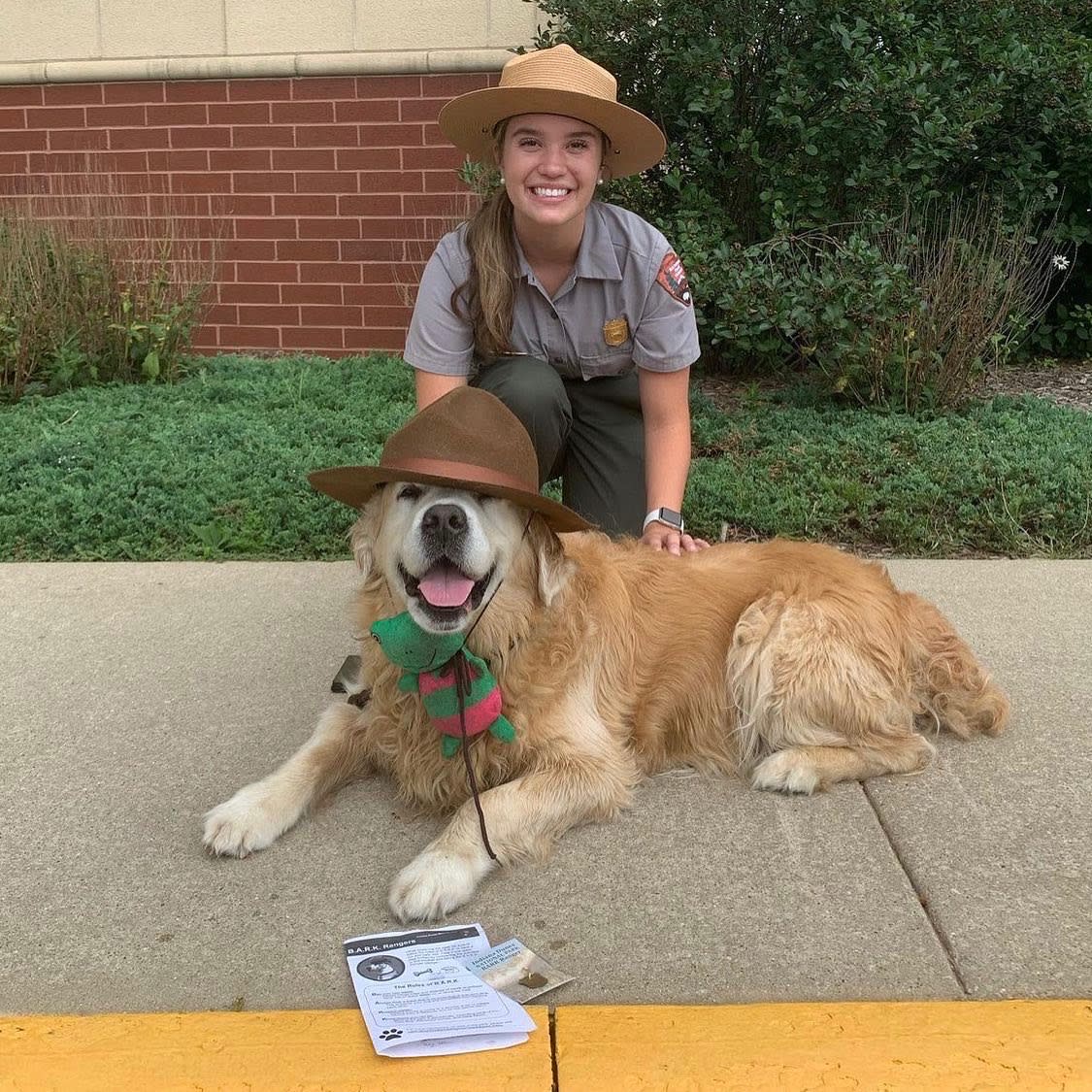 A dog with a park ranger hat sits in front of a park ranger