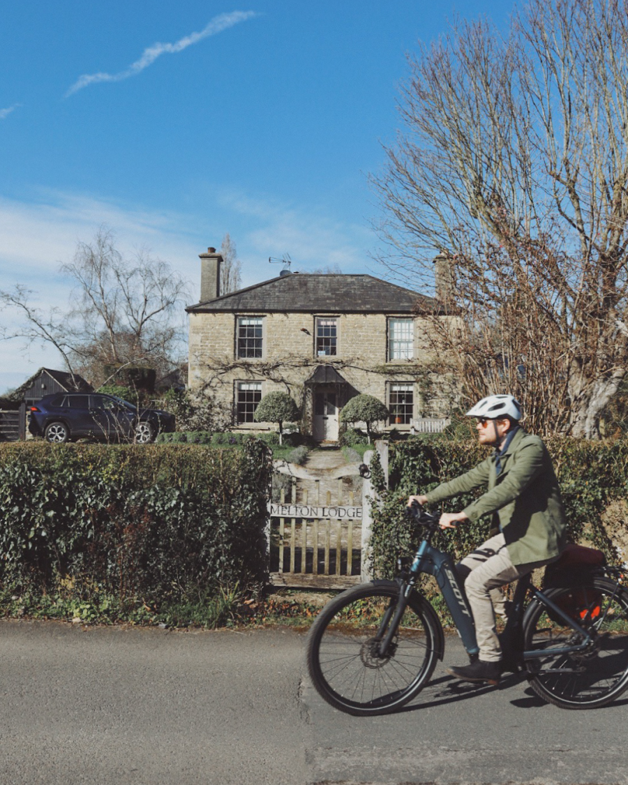 Tom cycling past a Cotswold stone house