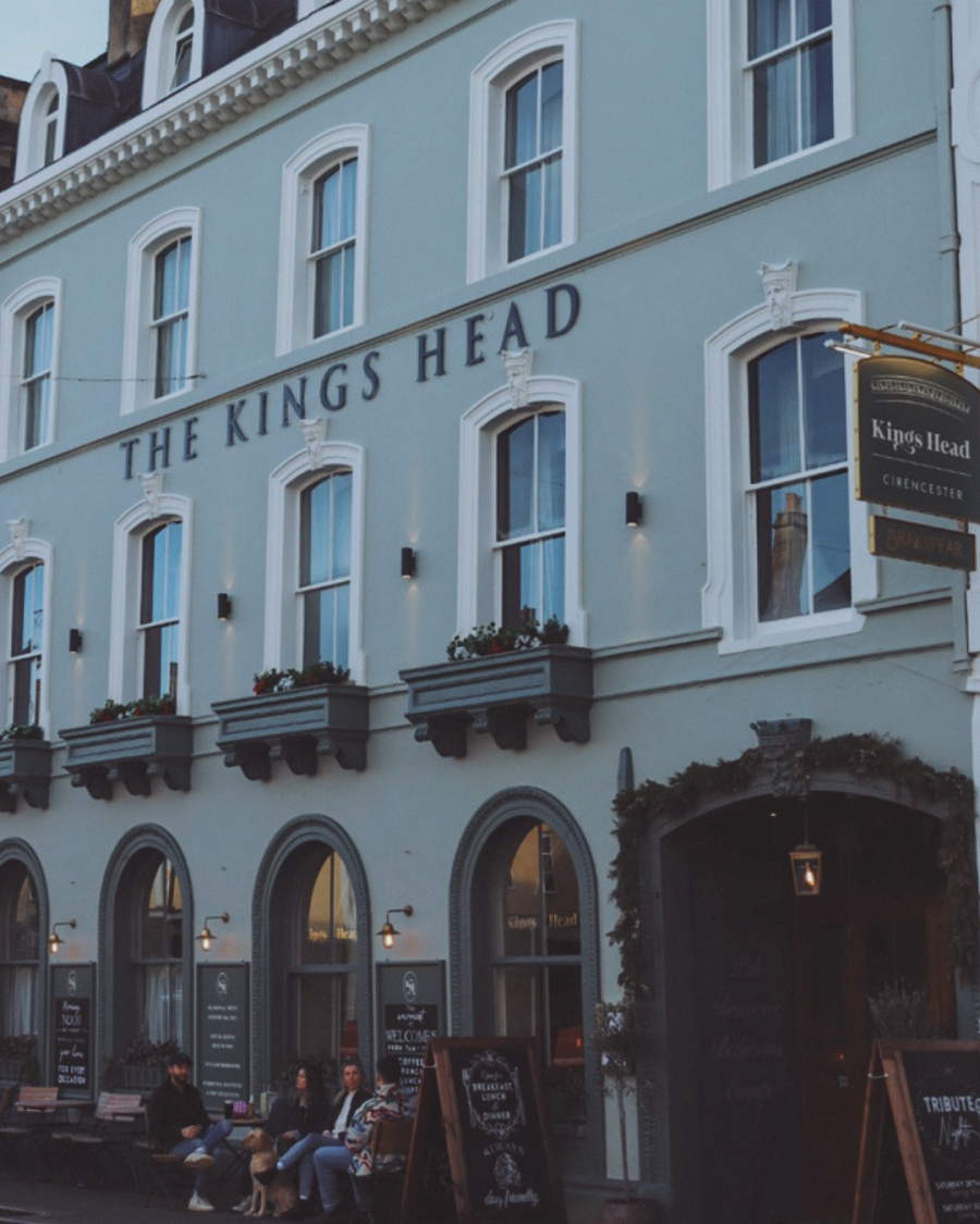 The front of The Kings Head in Cirencester, a pale blue building with white bordered windows and arched doorways