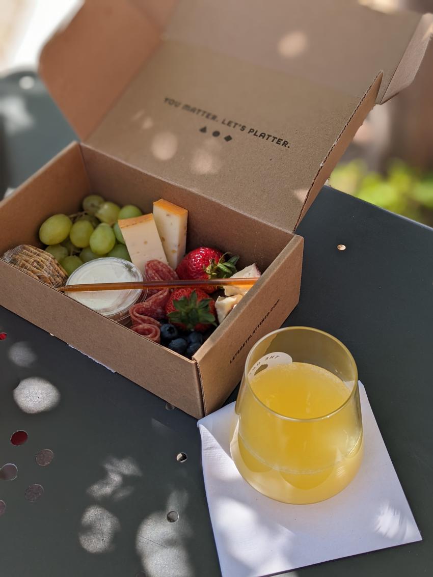 a charcuterie spread in a box with a cocktail next to it